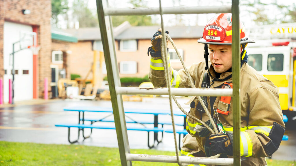 A firefighter behind a ladder outside a fire station