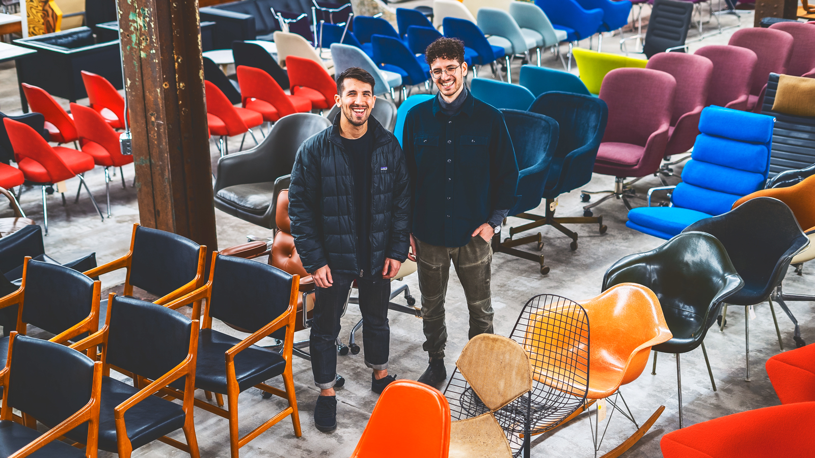 Jeremy Bilotti and David Rosenwasser stand among a warehouse filled with colorful furniture