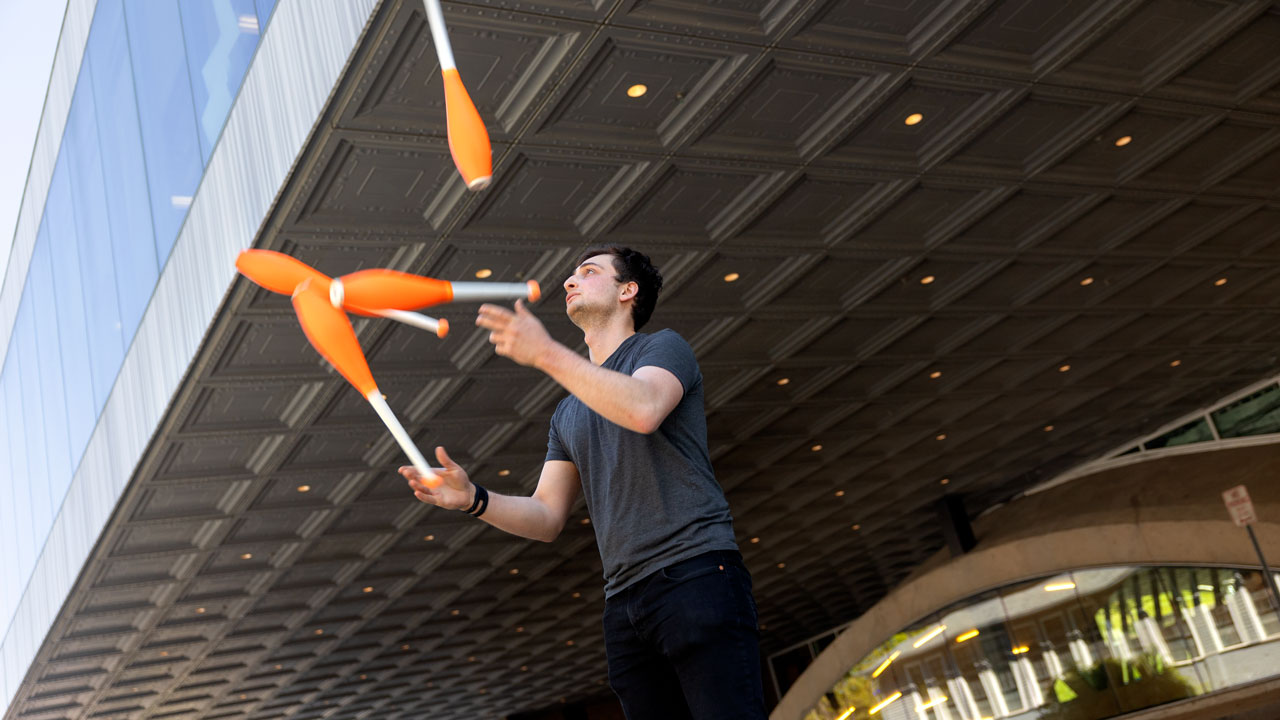 Jonah Botvinick-Greenhouse, math PhD student, juggles four orange clubs outside Milstein Hall.