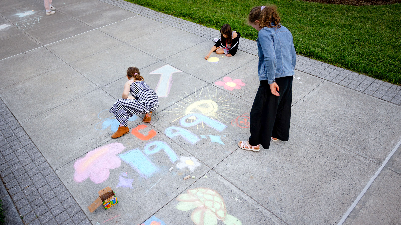 Children create chalk drawings on a campus sidewalk during Reunion 2024