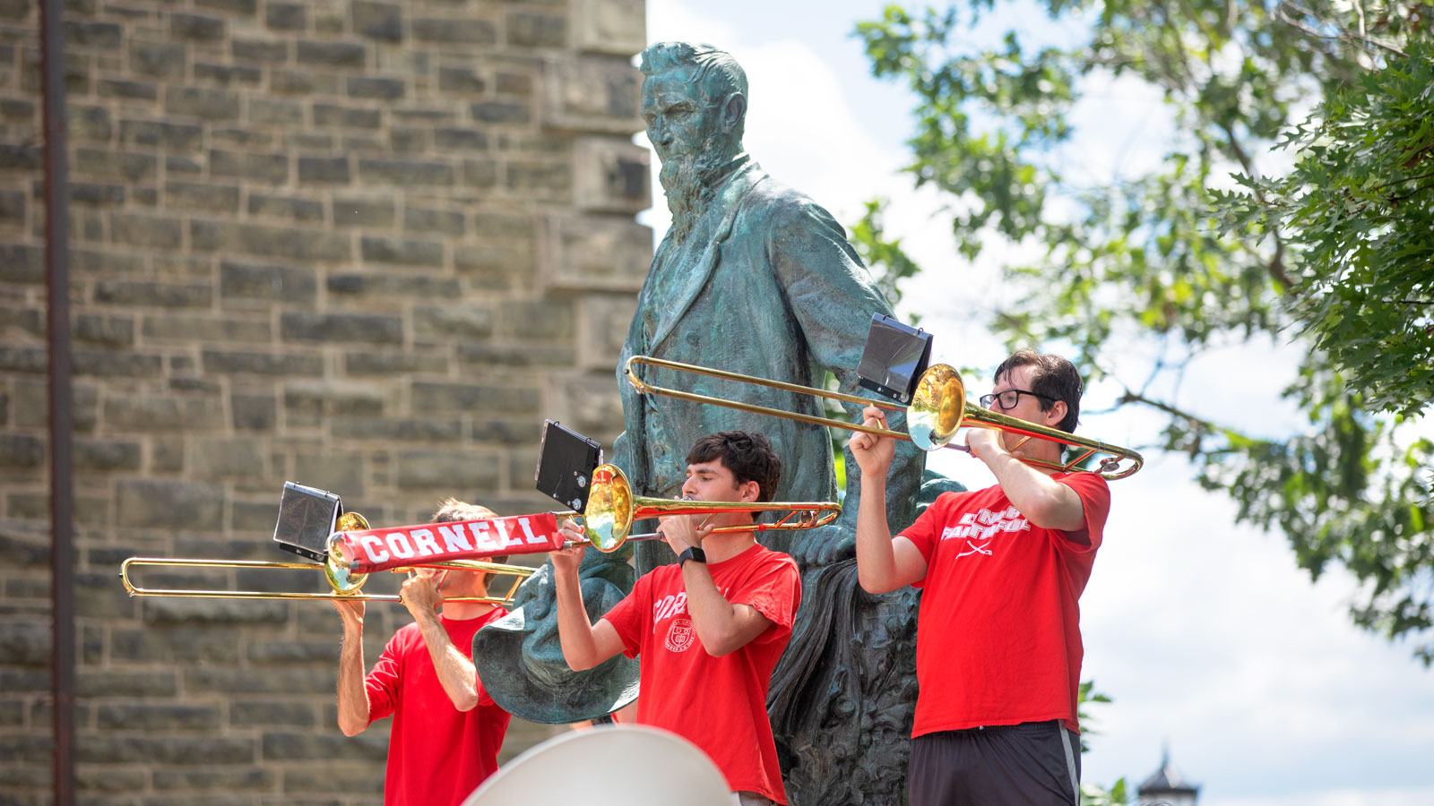 Members of the Cornell Big Red Band play trombones in front of the Ezra Cornell statue on the Arts Quad during Reunion 2024