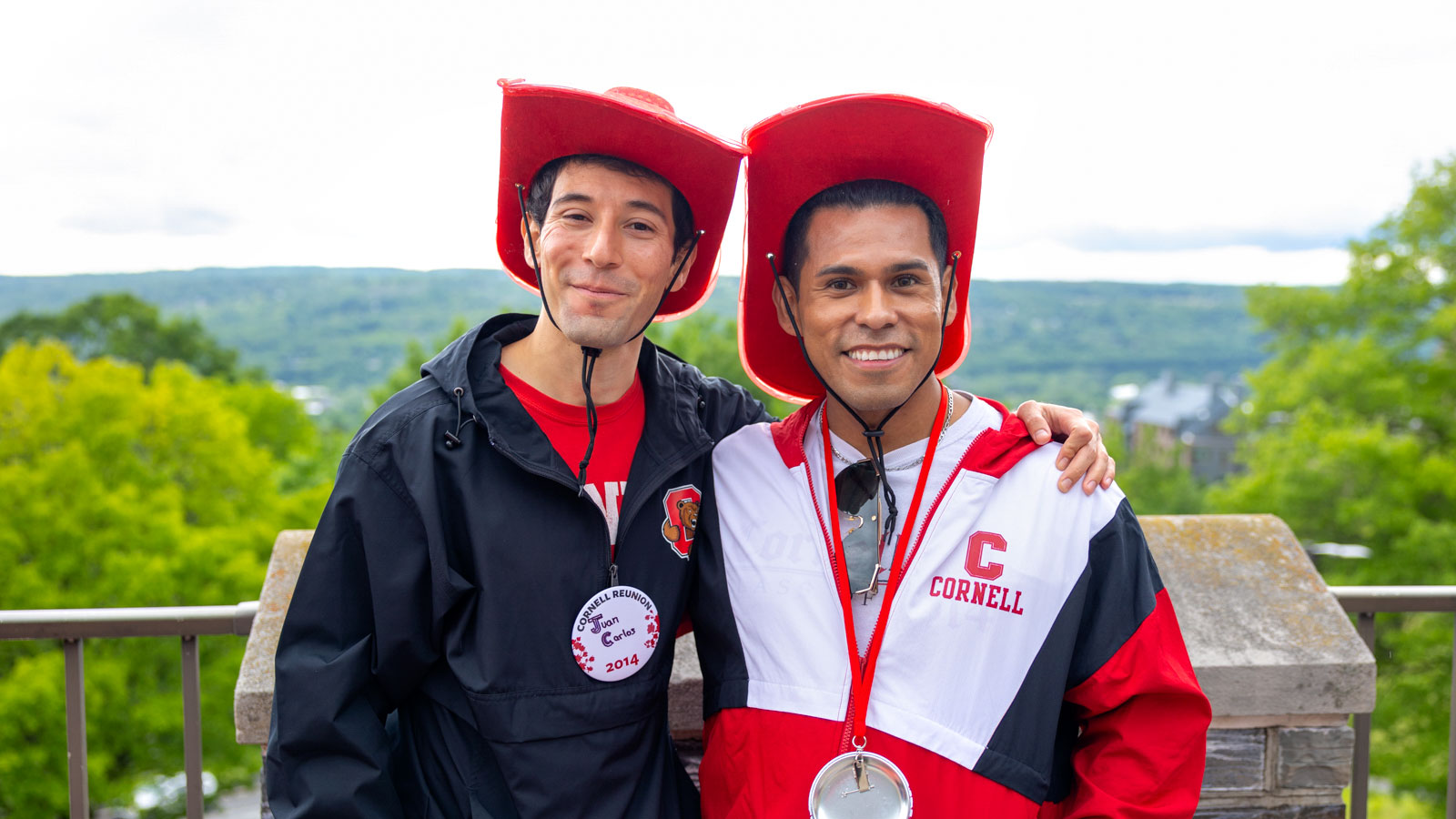 Two Cornellians wearing red “Cornellians” cowboy hats pose on the Willard Straight Terrace during Reunion 2024