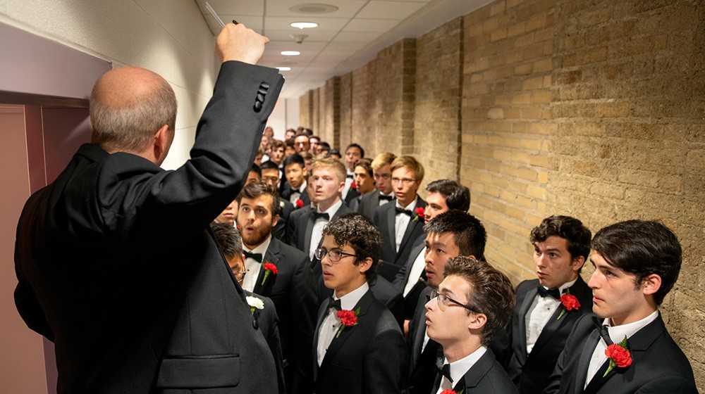 Robert Isaacs, assistant professor and Priscilla Browning Director of Choral Programs, leads members of the Glee Club in a warm up backstage.