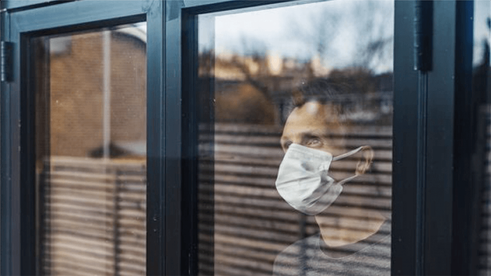 Man wearing a mask looking out window.